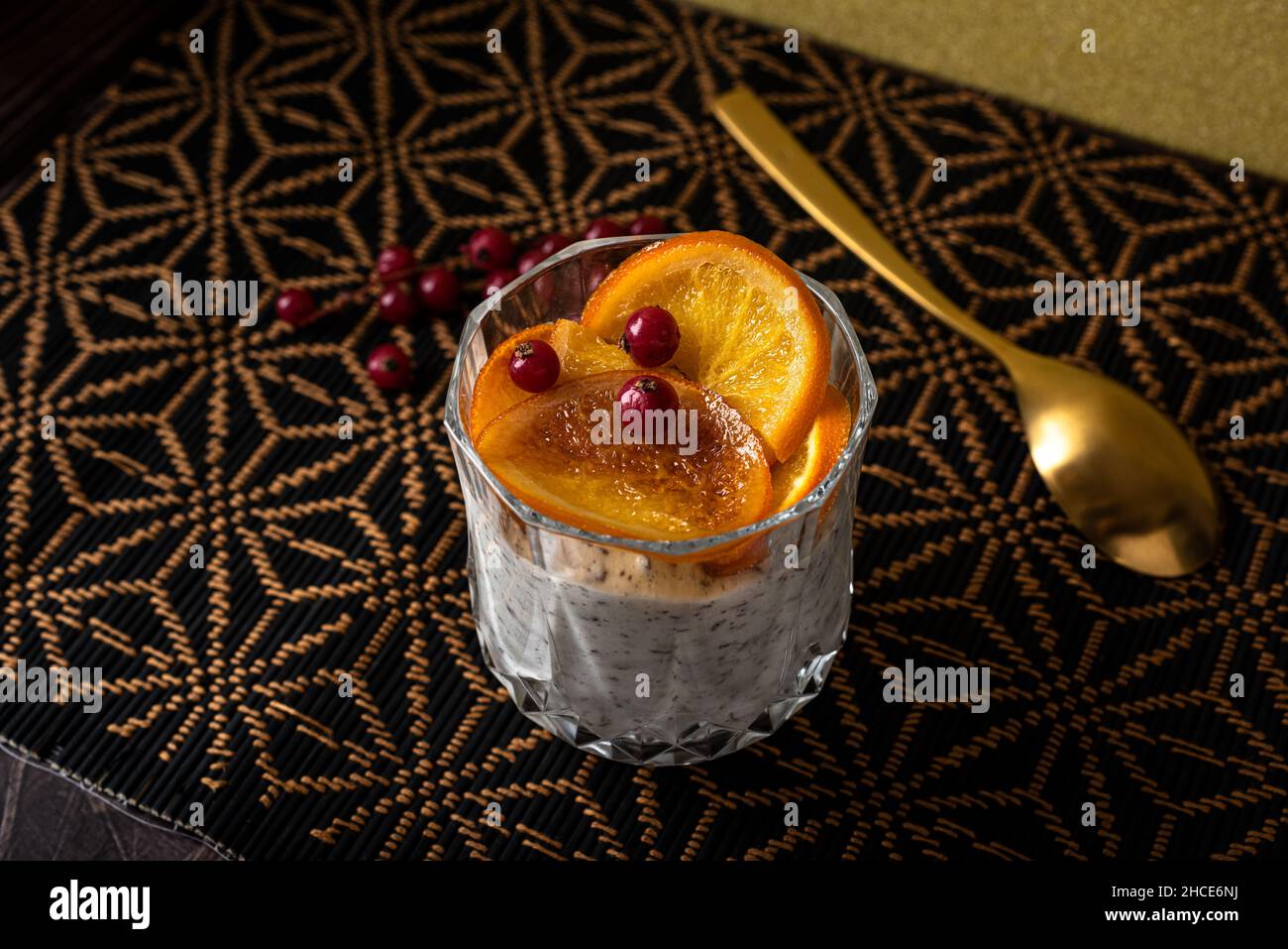 Alto angolo di calice di dessert a base di stracciatella mousse e scaglie di cioccolato sormontato da fette di arancia caramellate e frutti di bosco vicino al cucchiaio Foto Stock