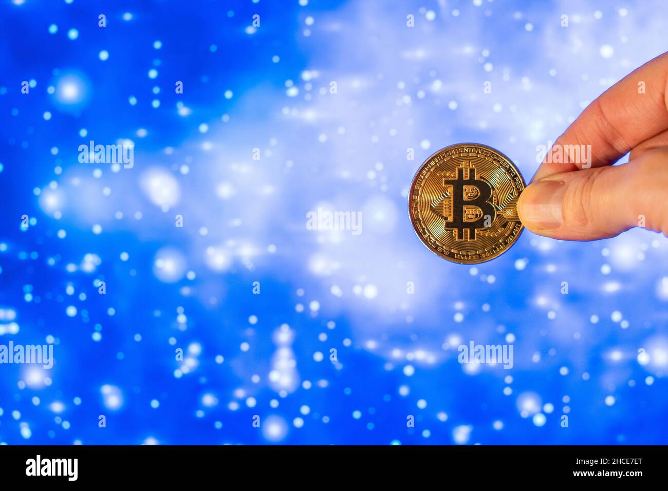 Ritagliare la mano dimostrando la moneta di bitcoin di metallo rotonda contro il brillante sfondo blu chiaro con macchie bianche Foto Stock