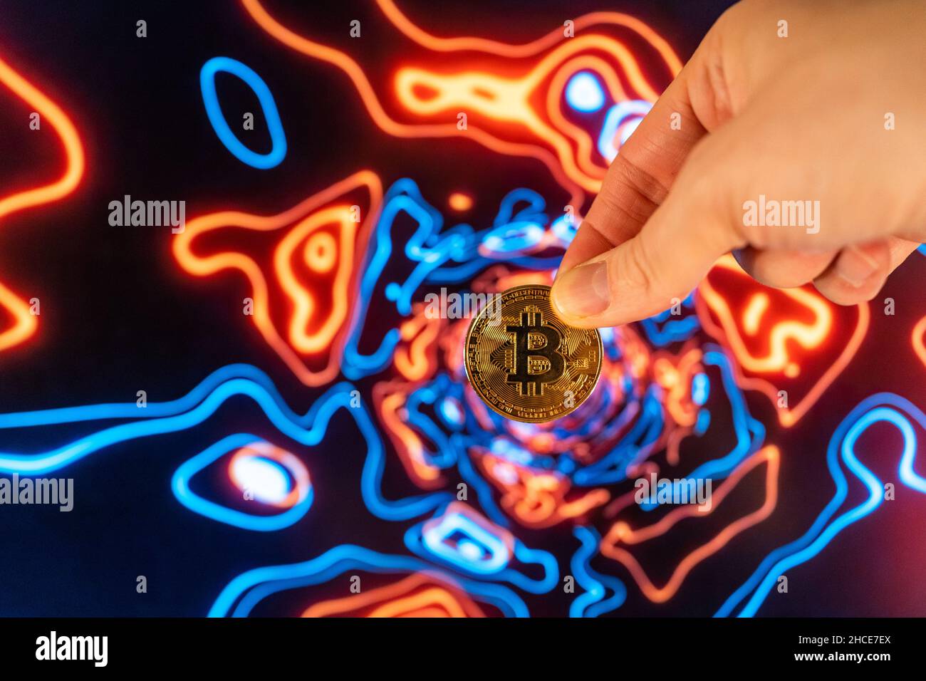 Ritagliare la mano che dimostra metallo moneta di bitcoin rotondo contro luce brillante sfondo colorato Foto Stock