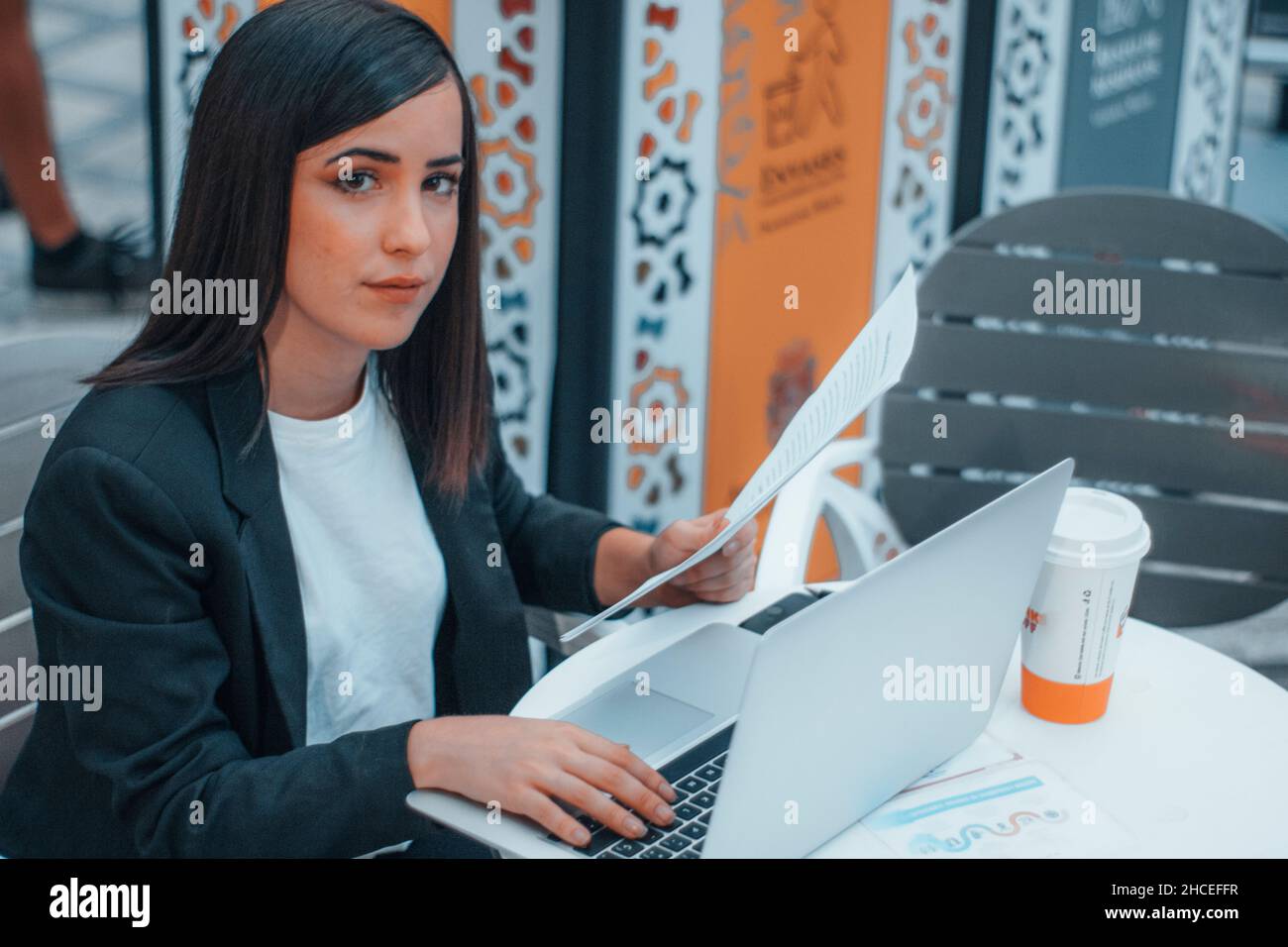 Giovane segretaria bruno-haired che rivede alcuni fogli di carta con i rapporti e le idee di affari per i suoi clienti in una città Foto Stock