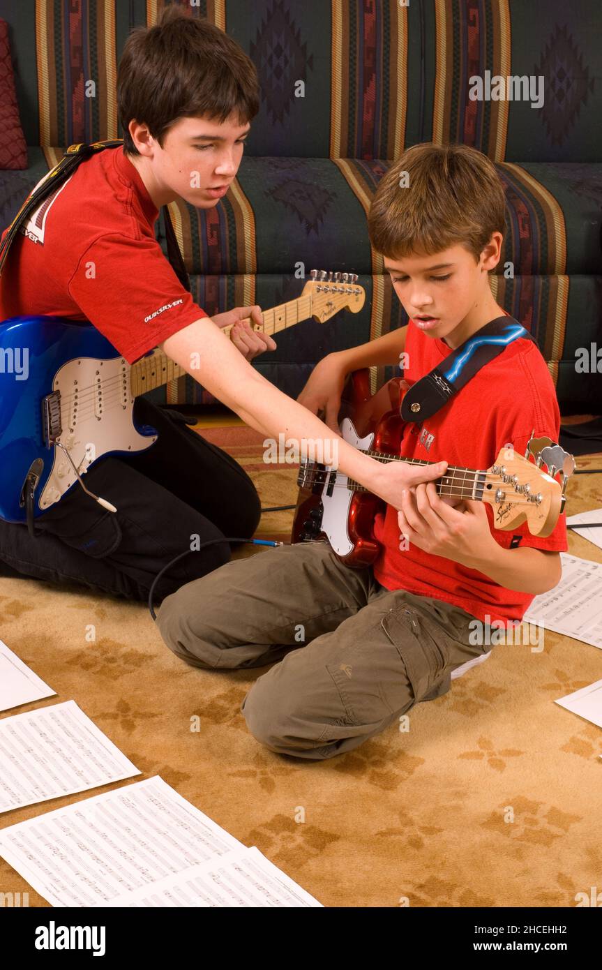 ragazzo di 13 anni a casa suonando la chitarra elettrica, suonando con il fratello di 12 anni, dimostrandogli accordo Foto Stock