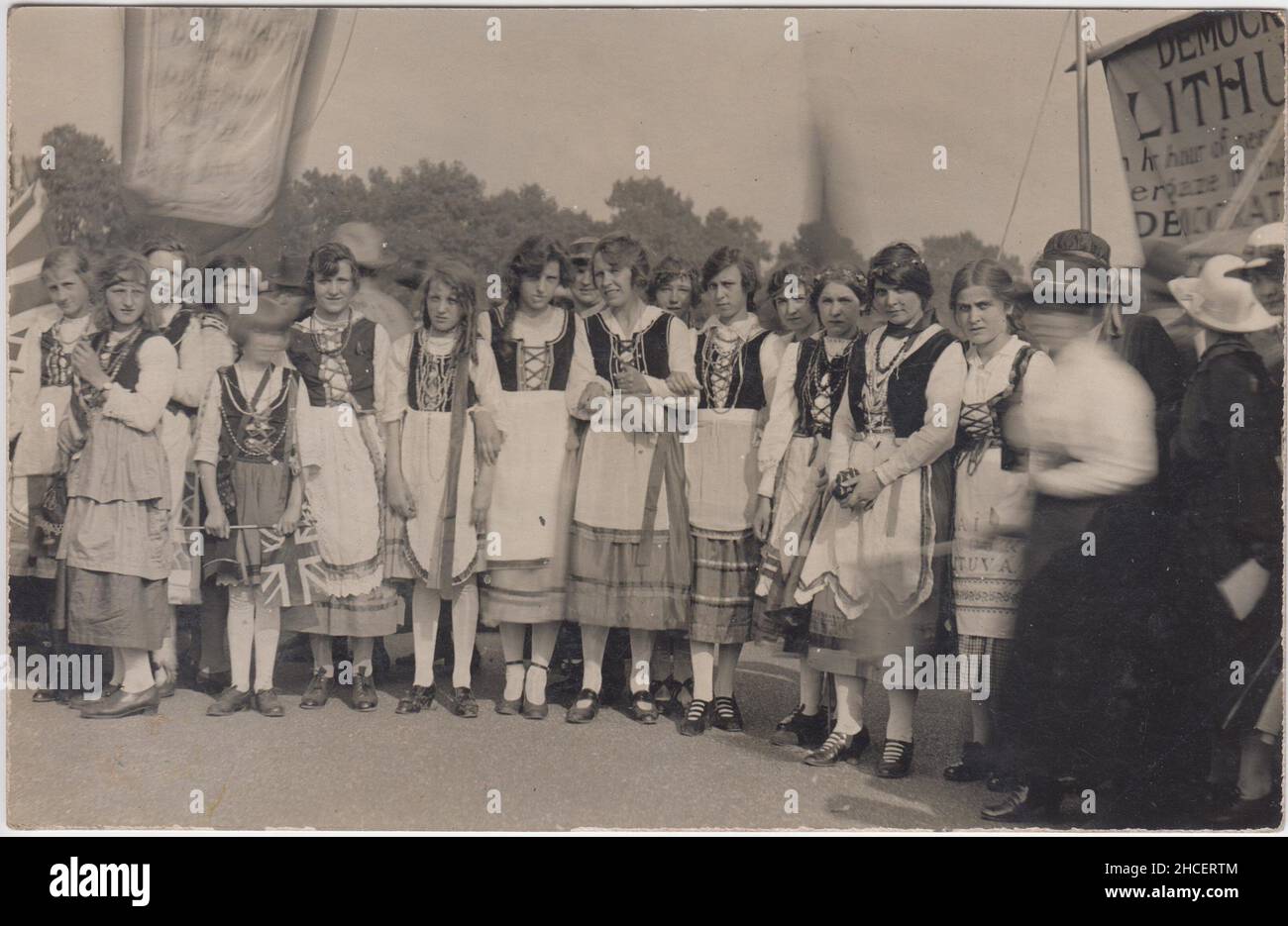 "Democrazia per la Lituania": Fotografia di una manifestazione per una Lituania indipendente e democratica tenutasi a Londra nel 1919. L'immagine mostra un gruppo di giovani donne e ragazze in abito nazionale lituano. Si possono vedere due striscioni, uno ha un titolo parzialmente oscurato "Lituania democratica” o "democrazia per la Lituania” e la frase "nel suo momento di bisogno”. Molte delle donne sono portatrici di bandiere Union Jack. La fotografia è stata scattata da Vere Holloway, fotografo, Ladbroke Grove, Notting Hill, Londra. Foto Stock