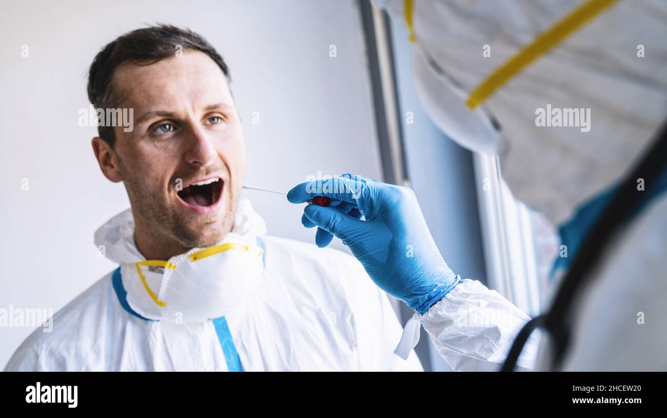 Il medico in abbigliamento protettivo prende la provetta con tampone dalla bocca di un medico esausto presso un centro di test Covid-19 durante l'epid del coronavirus Foto Stock