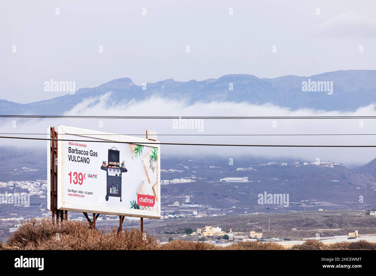 Billboard che fa pubblicità a gas BBQ dal negozio di hardware Chafiras sullo sfondo della montagna e con cavi elettrici che passano di fronte, Los Abrigos, Ten Foto Stock