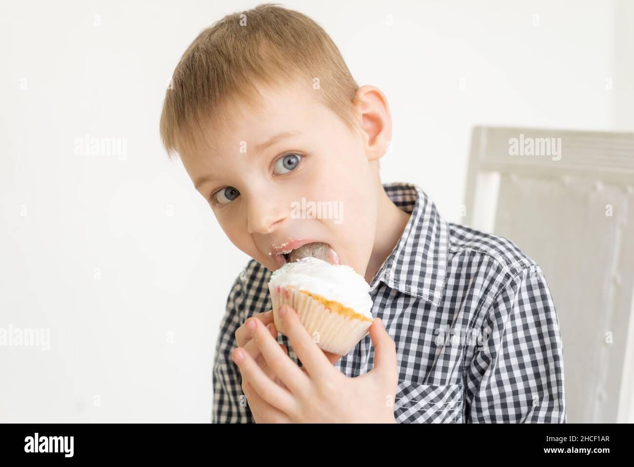 Un ragazzo in una camicia mangia una torta su uno sfondo chiaro. La gioia del cibo dei dolci. Foto Stock