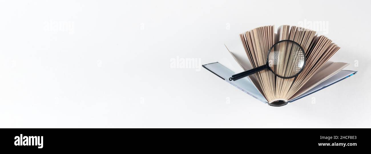 Lente di ingrandimento sopra il libro di carta aperto. Concetto di conoscenza, ricerca e studio. Banner con spazio di copia. Foto Stock