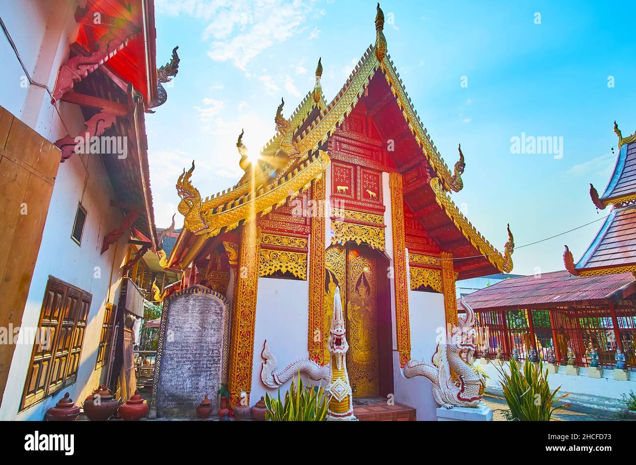 I luminosi raggi del sole brillano sul tetto del Gable dell'Ubosot di Wat Muen Ngoen Kong, decorato con bargeboards intagliati dorati e serpenti Naga, Chiang M. Foto Stock