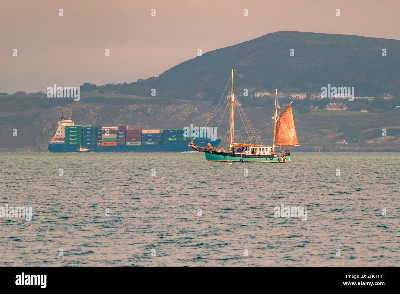 Sandycove, Dublino, Irlanda, 13 novembre 2021: Un piccolo yacht nella baia di Dublino con una nave container sullo sfondo. Foto Stock