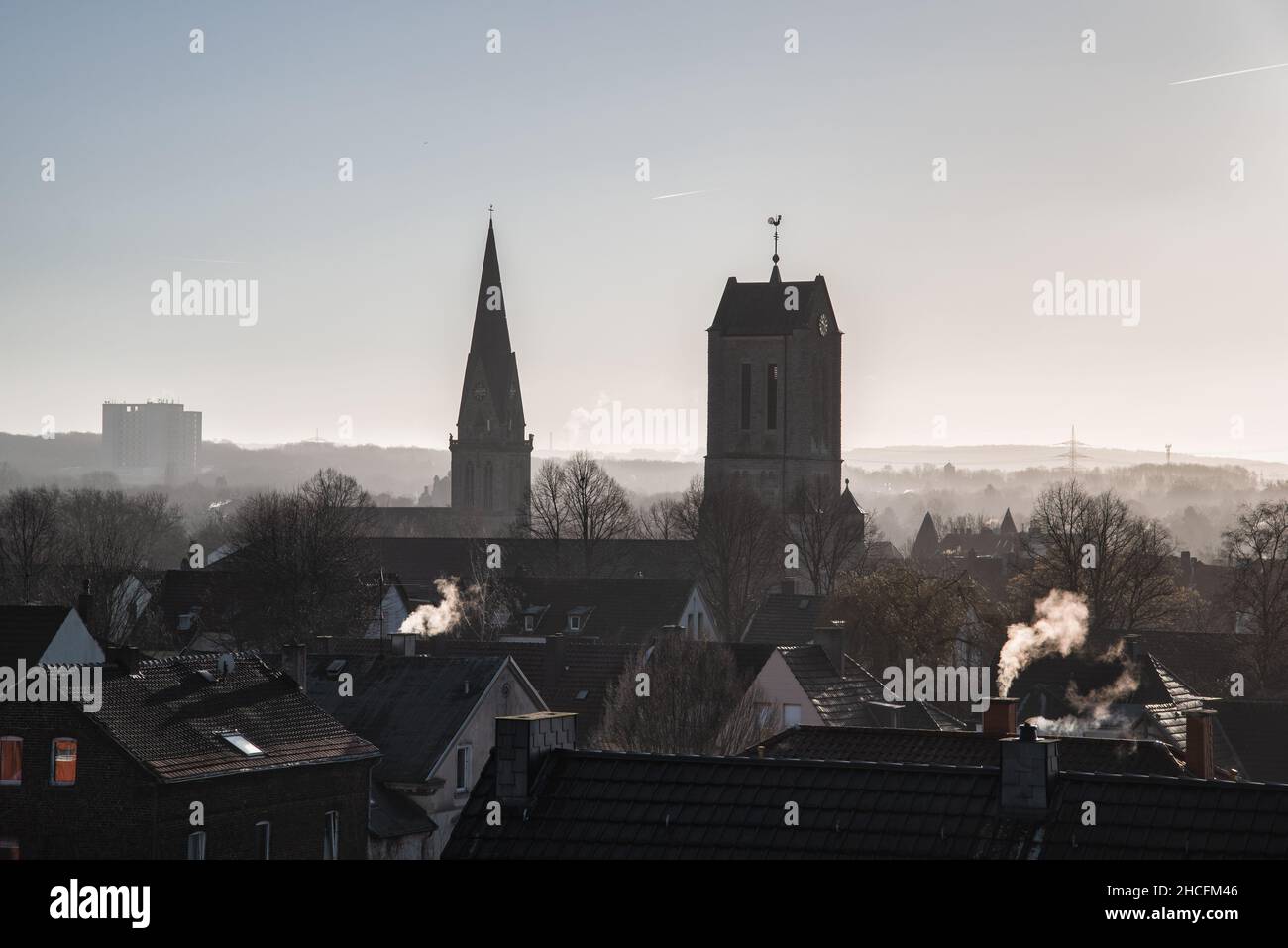 Vista sui tetti di Bochum Langendreer in Germania con le due chiese e l'ospedale universitario in sfondo nebbia. Camini fumatori. Foto Stock