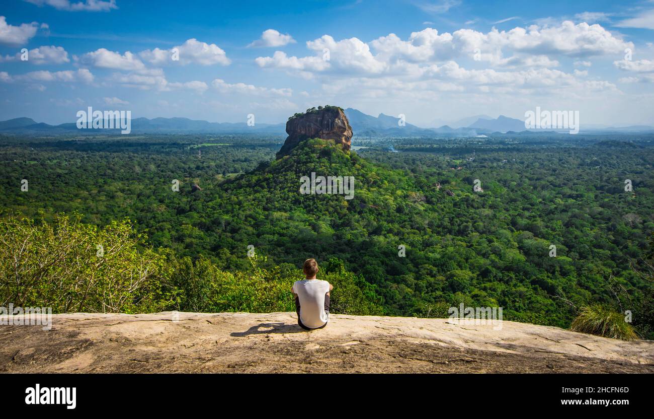 Escursionista seduto su una collina rocciosa e guardando la Sigiriya circondato da foreste in Sri Lanka Foto Stock