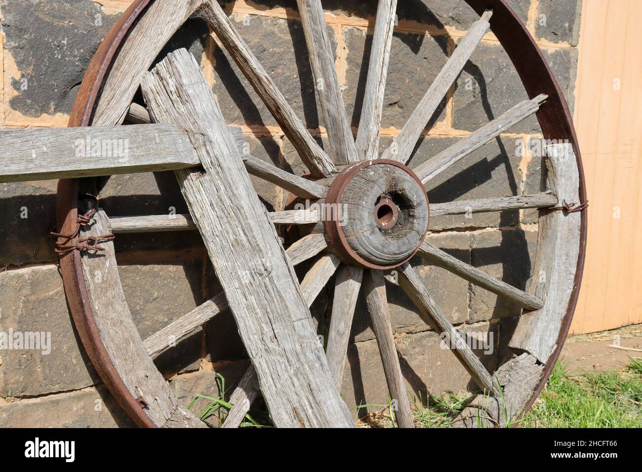 Antica ruota carrozza in legno con bordo in metallo appoggiato a un muro in pietra Foto Stock