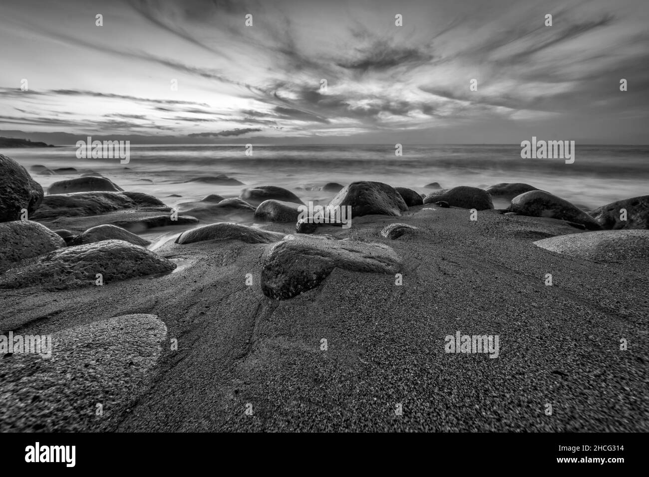 Un Ocean Seascape Sunset Sky con un dettagliato Moody Cloudscape come una dolce onda rotola a Shore in bianco e nero immagine formato Foto Stock
