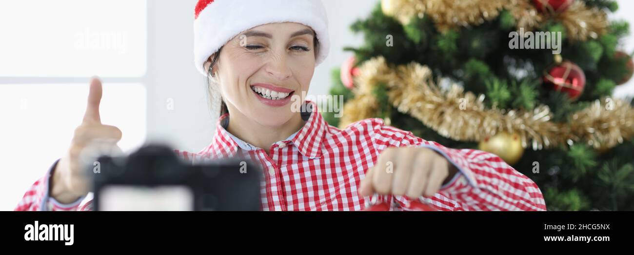 Giovane donna blogger in babbo natale cappello tiene sveglia e verricelli alla macchina fotografica Foto Stock