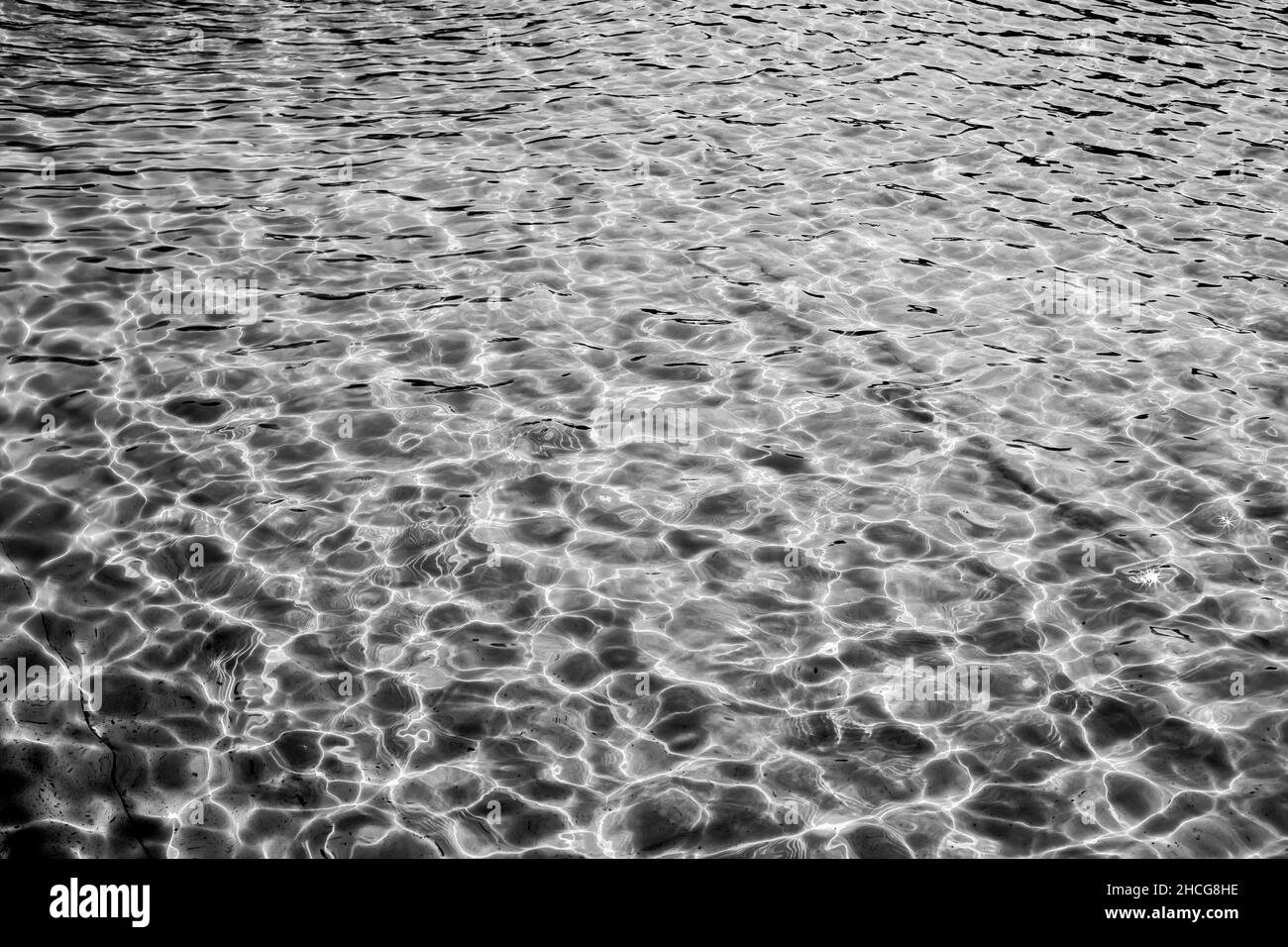 Acqua bianca e nera con riflessi solari chiari, ondulazione leggera sulla superficie dell'acqua e raggi solari Foto Stock