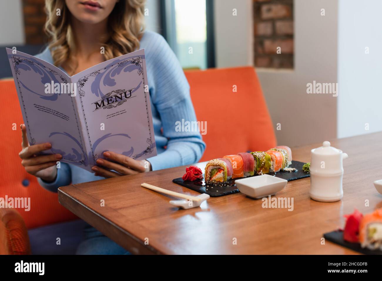 vista ritagliata del menu di lettura della donna sfocata vicino a gustosi sushi rotolini sul tavolo Foto Stock