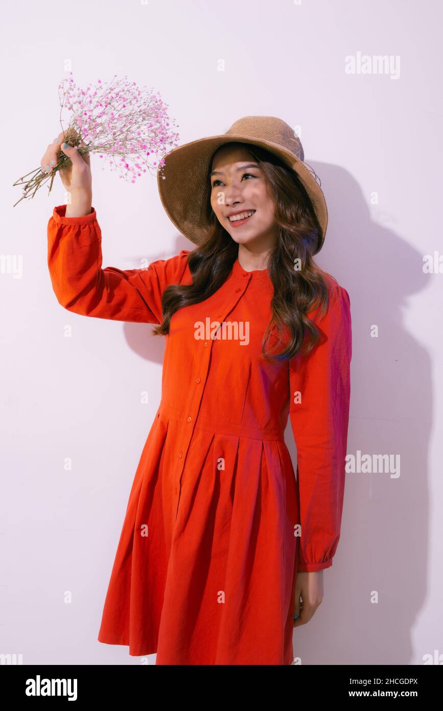 Giovane donna in cappello di paglia e abito rosso che tiene fiori rosa su rosa Foto Stock