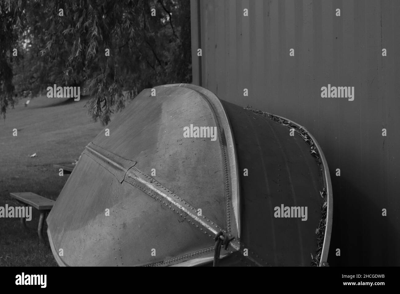 Foto in scala di grigi di una vecchia barca vicino alla casa sul lago Foto Stock