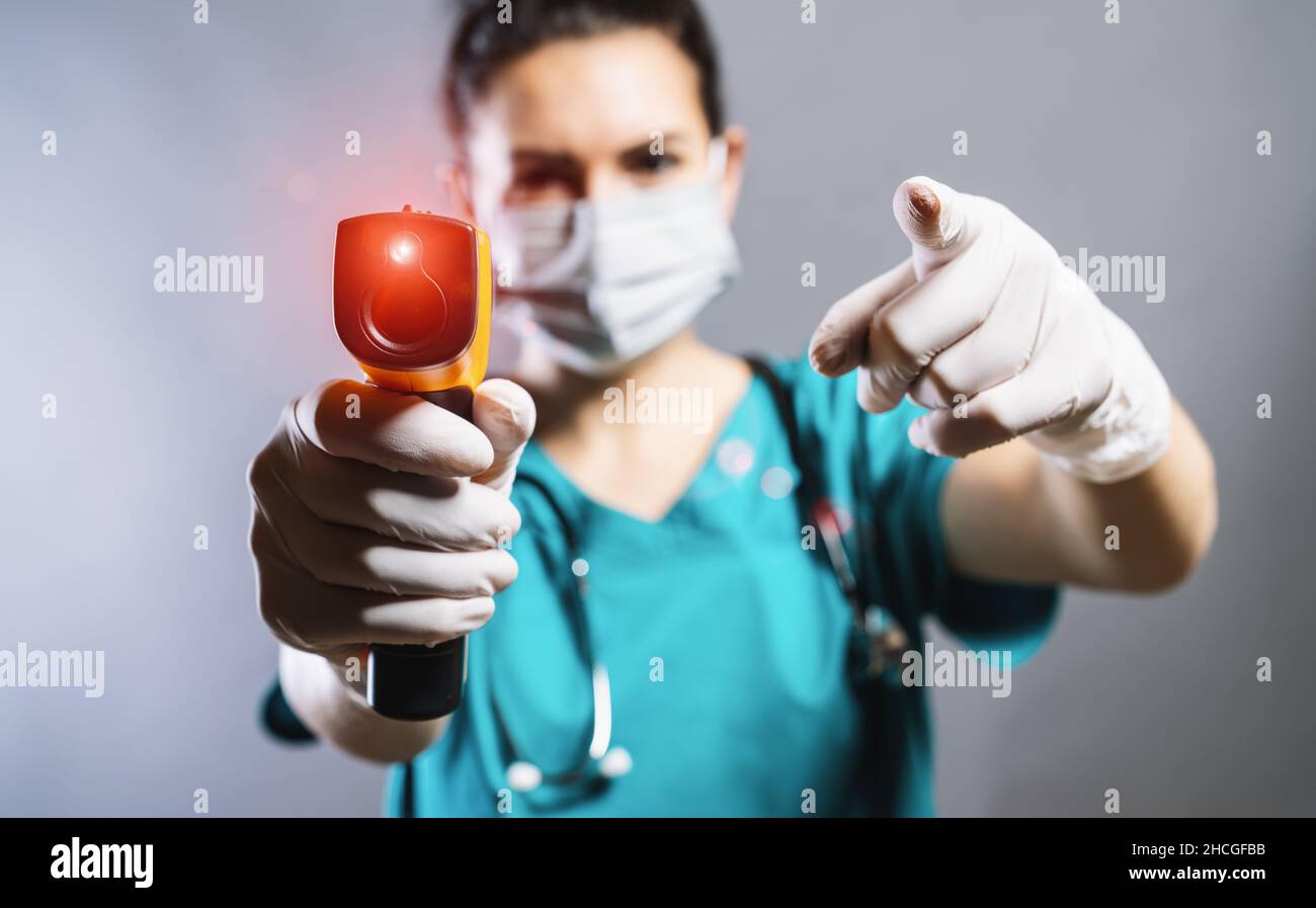 Medico che indossa maschera chirurgica protettiva pronto all'uso termometro ad infrarossi per la fronte (termometro a pistola) per controllare la temperatura corporea per il virus corona COVID- Foto Stock