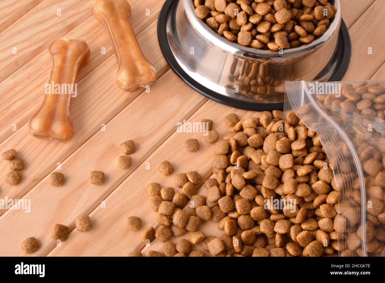 Crocchette di cani in sacchi e alimentatore su tavola di legno con ossa della pelle pressate. Vista rialzata. Composizione orizzontale. Foto Stock