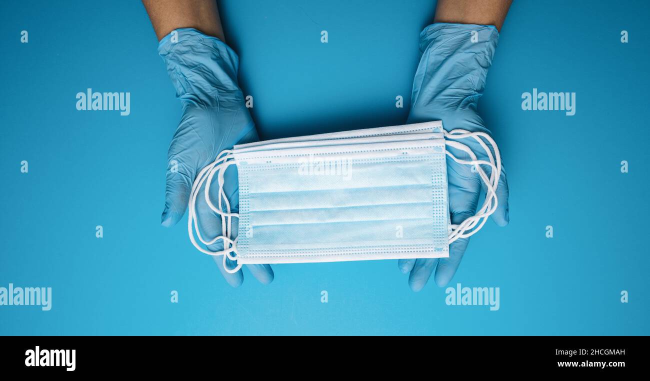 Mani in guanti che mostrano molte maschere mediche su sfondo blu. Misure preventive per la protezione contro l'infezione da virus di Corona Covid-19. Foto Stock