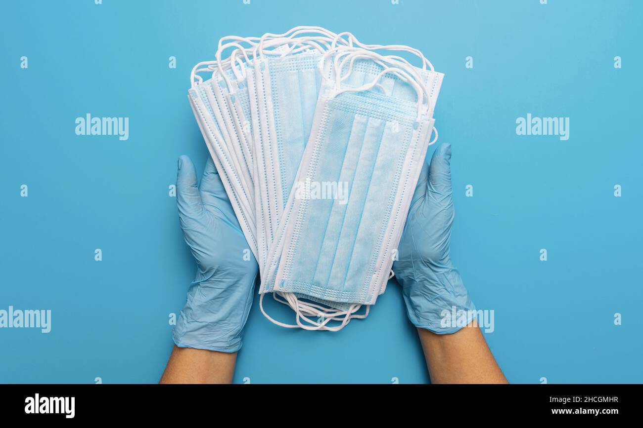 Mani in guanti che mostrano molte maschere mediche su sfondo blu. Misure preventive per la protezione contro l'infezione da virus di Corona Covid-19. Foto Stock