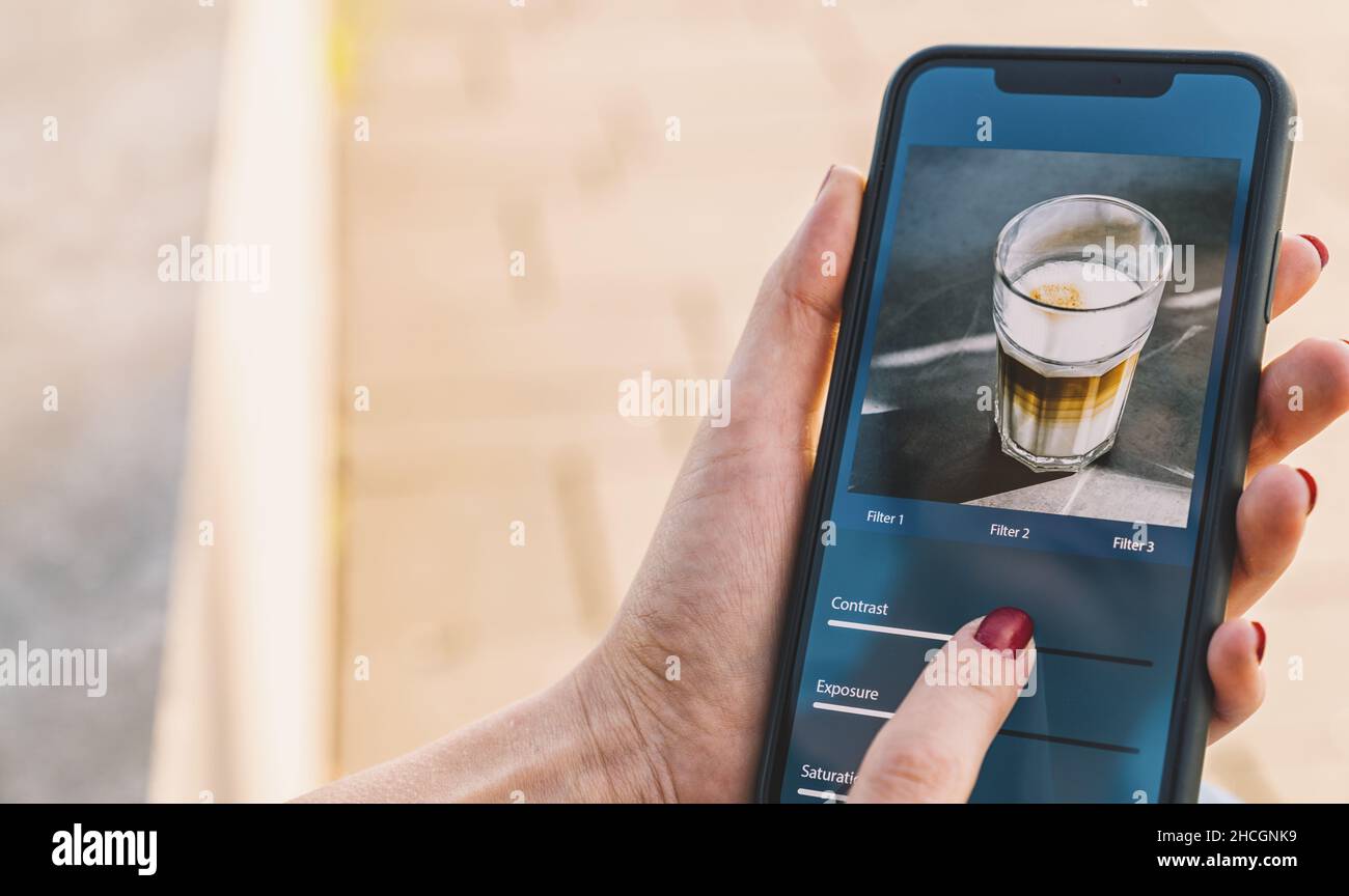 Editing di foto con telefono cellulare e app smart. Donna che regola i cursori. Modifica, manipolazione, miglioramento o miglioramento delle immagini con lo smartphone. Aggiunta di f Foto Stock