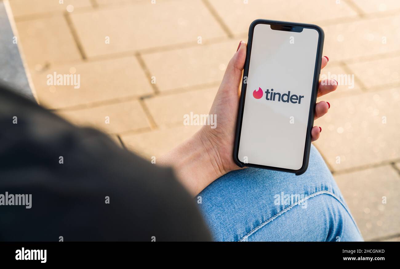 Donna che tiene in mano iphone X con il logo dell'app Tinder per effettuare l'accesso. Tinder è un'applicazione di localizzazione di persone multipiattaforma per incontri romantici online. Foto Stock