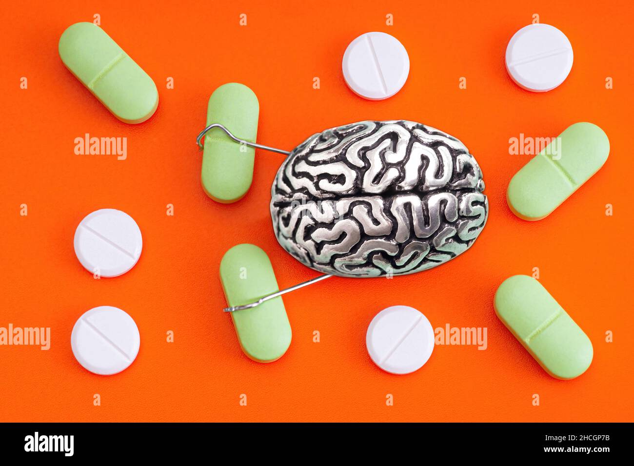 Copia anatomica di un cervello umano con mani che afferrano pillole su sfondo arancione. Concetto di tossicodipendenza. Foto Stock