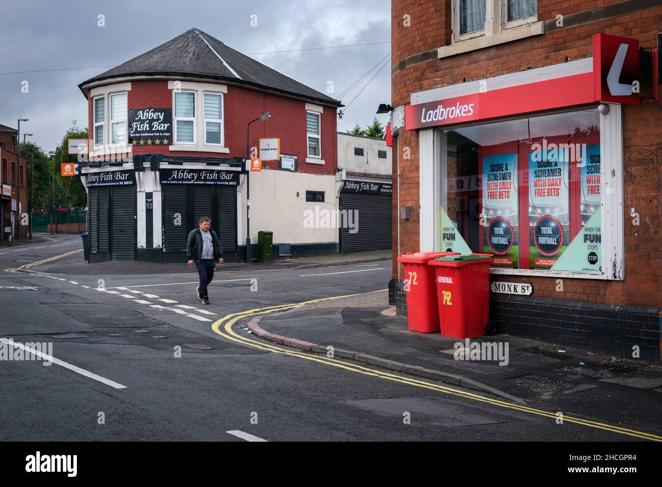 Una scena di strada in un'area cittadina interna di Derby con un negozio di fish and chip e un negozio di scommesse agli angoli della strada, Derby, Inghilterra Foto Stock