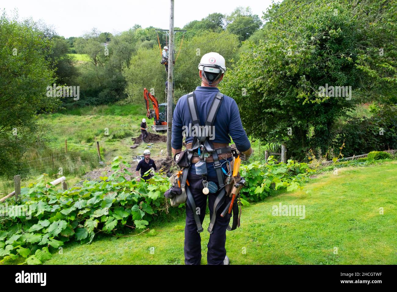 Operai di elettricità che lavorano con le attrezzature e la scavatrice che mettono in su la nuova linea dell'asta di servizio in estate Carmarthenshire Galles Regno Unito Gran Bretagna KATHY DEWITT Foto Stock