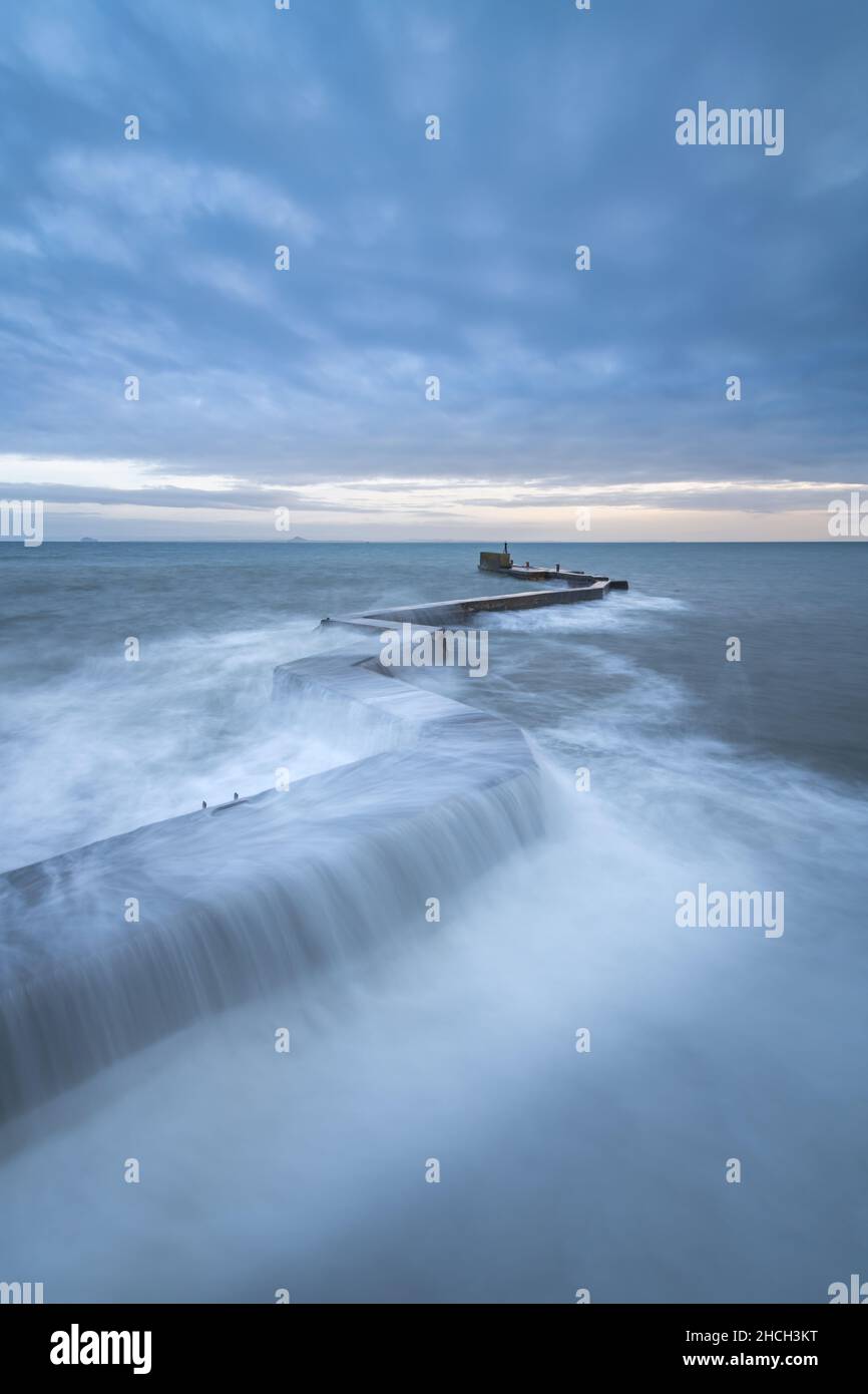 Onde che si infrangono sull'iconico frangiflutti a zig-zag al porto di St Monans nel Neuk orientale di Fife, Scozia, Regno Unito. Foto Stock