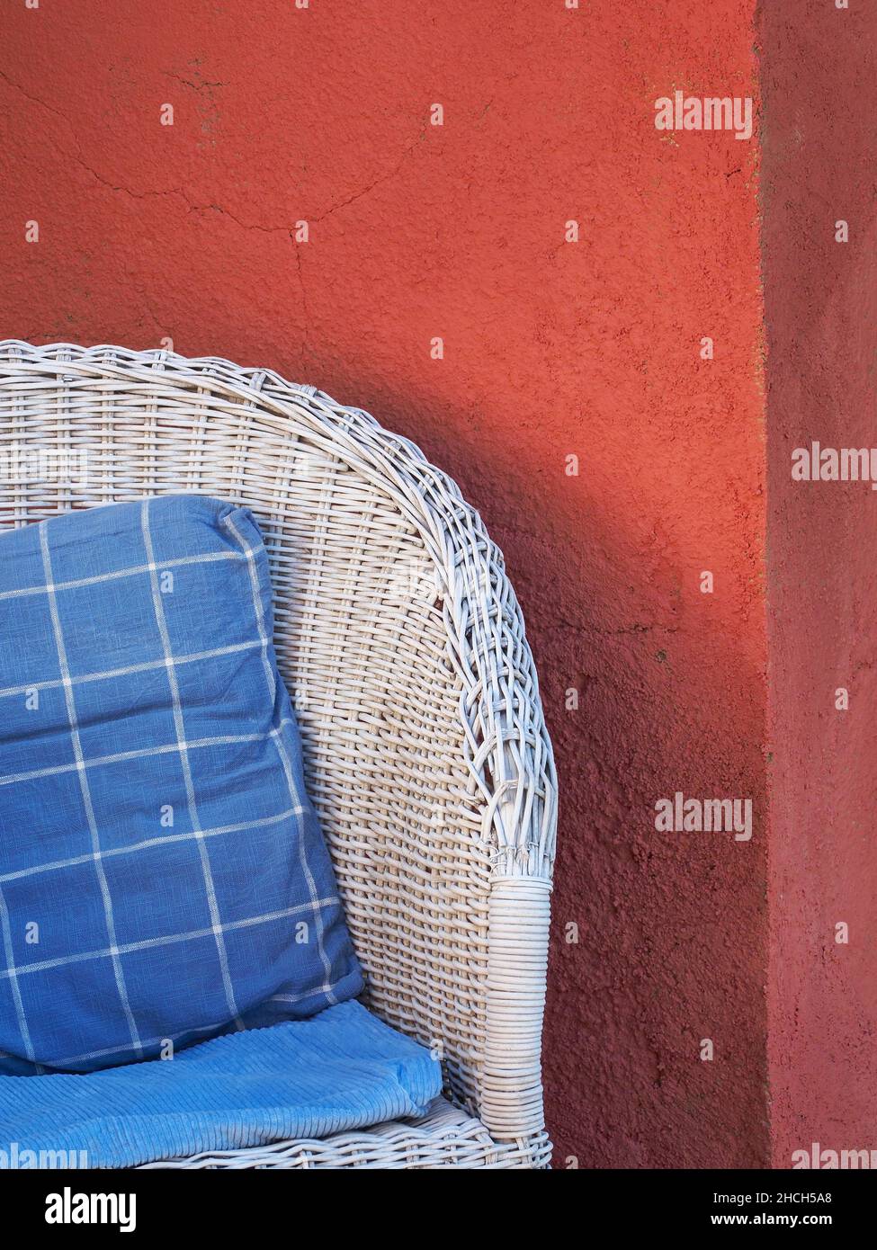 Sedia in vimini bianca con cuscino di colore blu e bianco davanti alla parete rossa Foto Stock