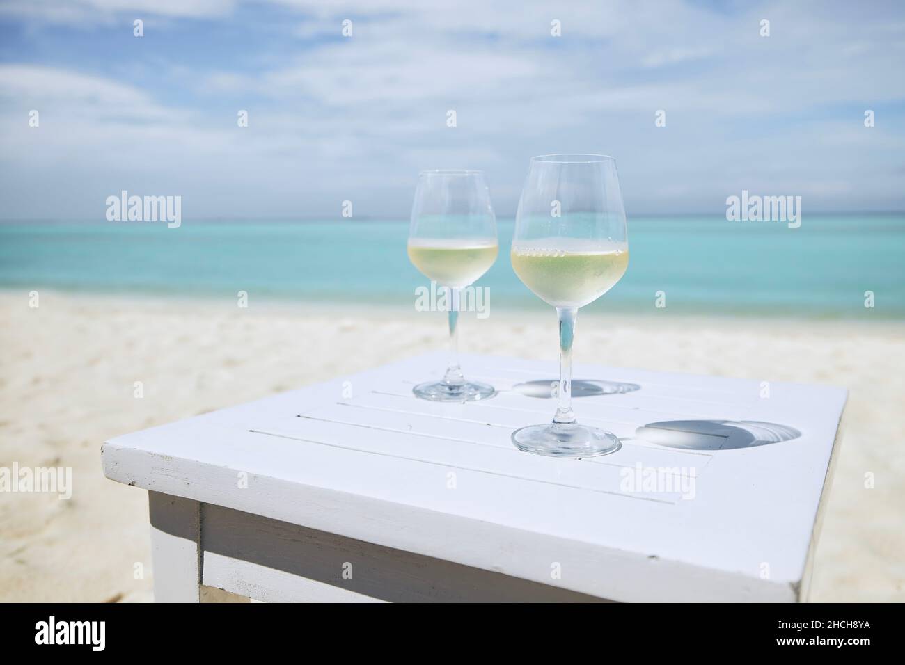 Due wineglass con vino bianco su tavola di legno contro idilliaca spiaggia e mare turchese. Foto Stock