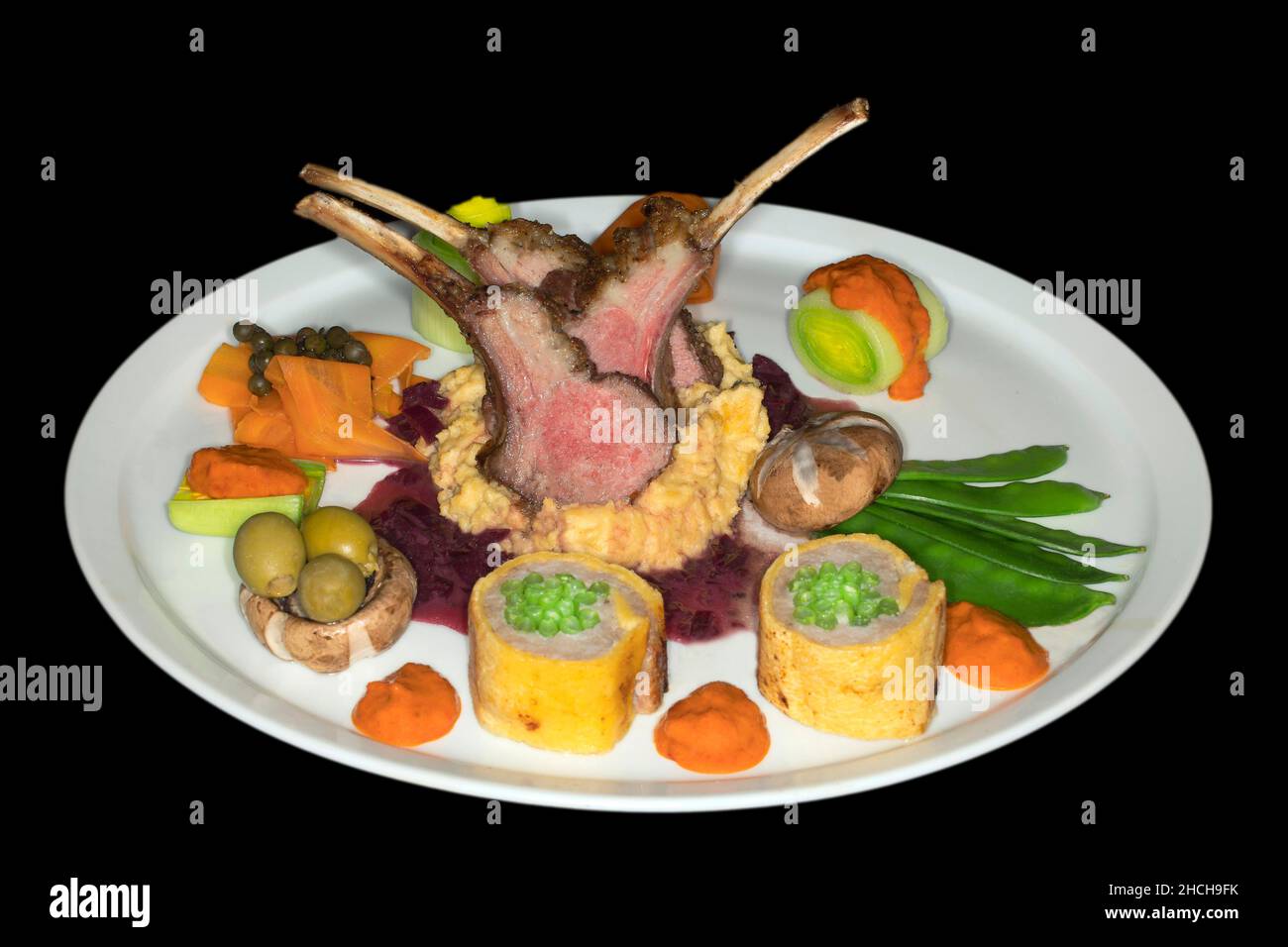 Sella di agnello arrosto rosa su polenta di mais con cipolle rosse, salsa di prezzemolo e verdure varie, fotografia da studio con sfondo nero Foto Stock