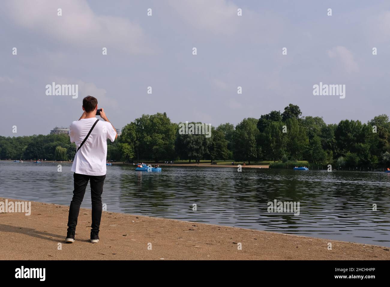 Giovane uomo con ritorno alla macchina fotografica fotografando barche da diporto su Hyde Park Serpentine London UK. Foto Stock