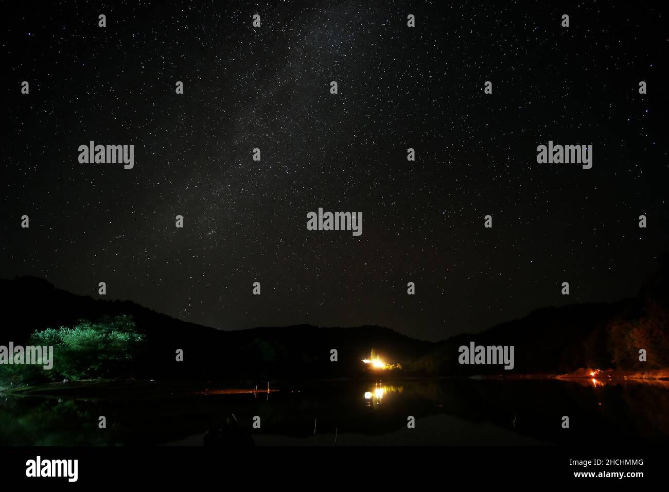 Serenità della notte stellare scura, con un fuoco sotto il via lattiginosa che illumina la luce bianca e setosa dal cielo Foto Stock
