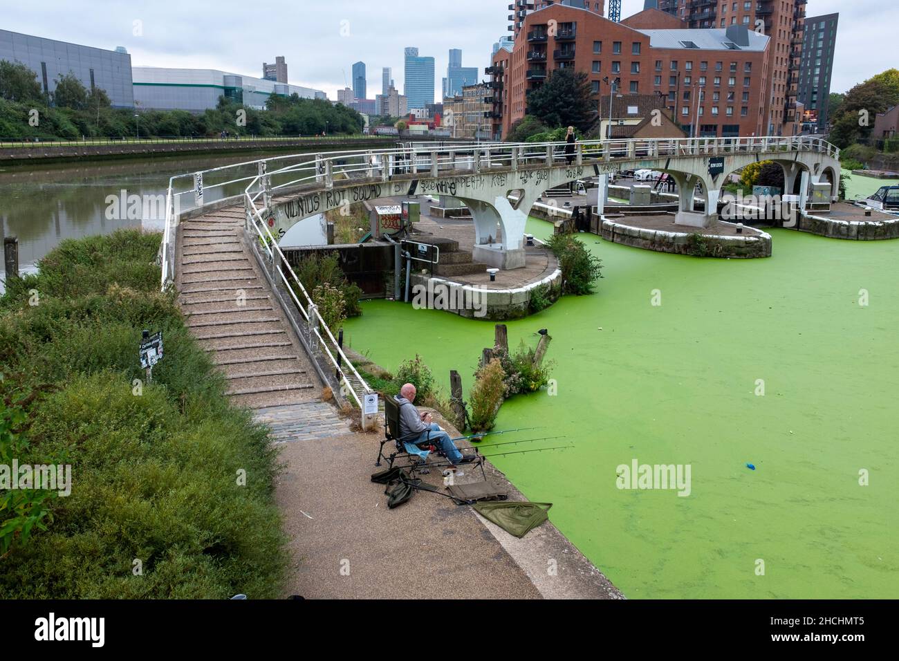 Uomo che pesca in Limehouse tagliare a serrature in Bow Creek. 'Vilnius Riot Squad' grafitti sul ponte sopra le serrature. Foto Stock