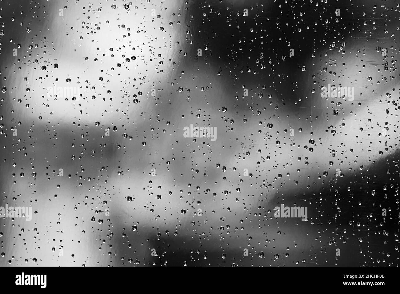 Scatto in scala di grigi delle gocce di pioggia sulla superficie di vetro Foto Stock