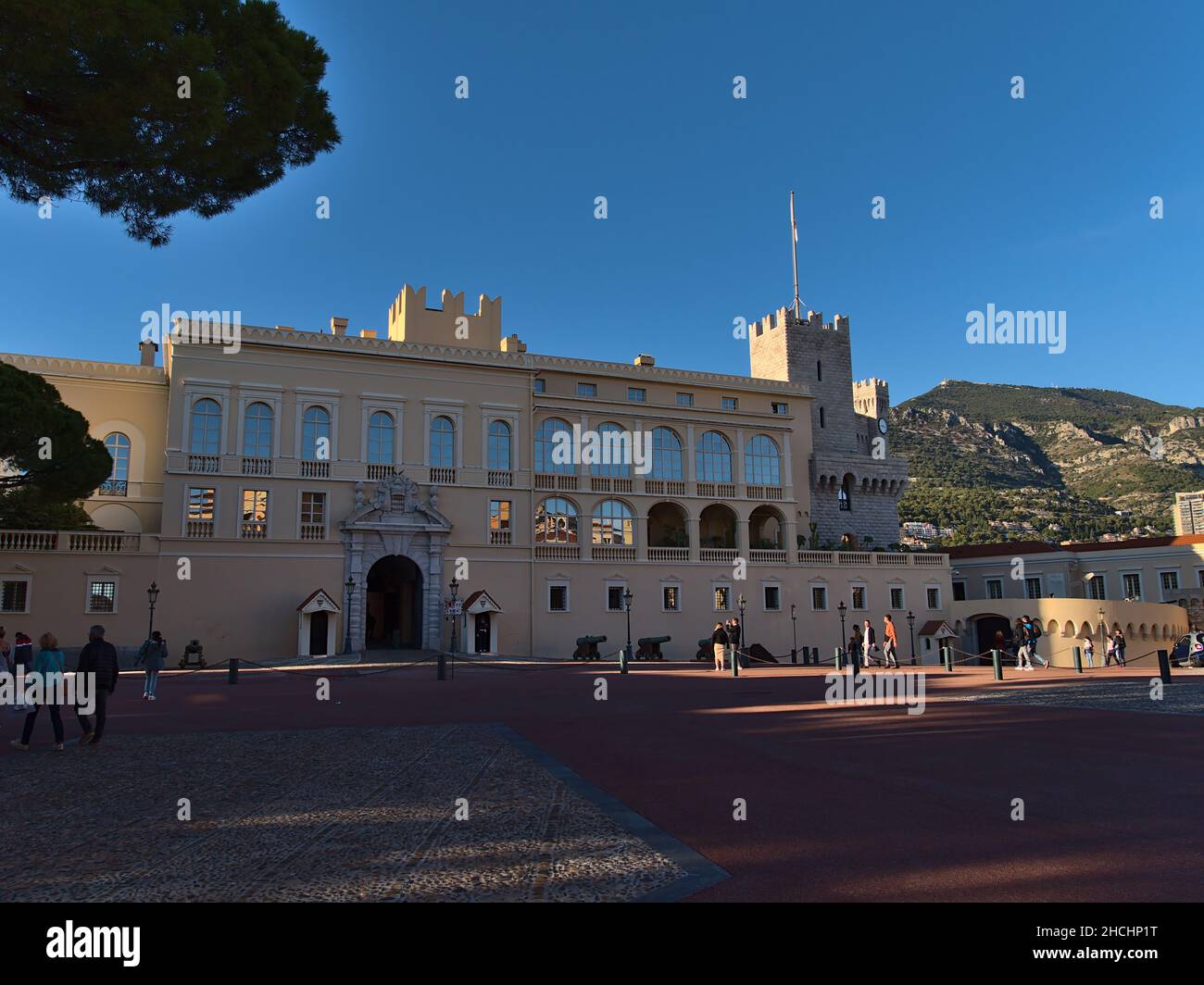 Vista sul famoso Palazzo del Principe di Monaco, la residenza ufficiale del Principe Sovrano, nel pomeriggio con turisti che camminano per e montagne. Foto Stock