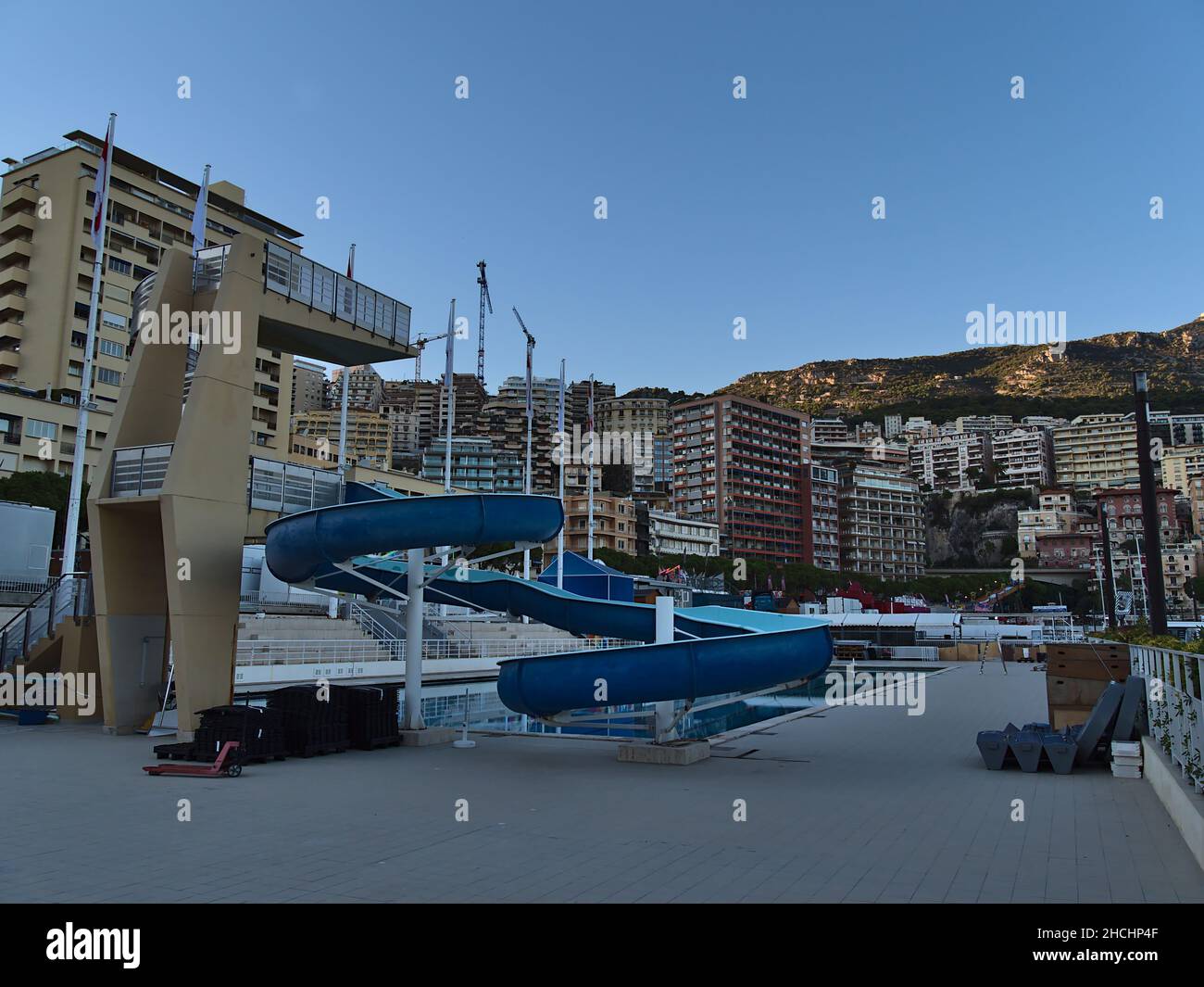 Scivolo d'acqua blu e trampolino di lancio allo Stadio nautico Rainier III nel centro di Monaco in serata con edifici residenziali alti. Foto Stock