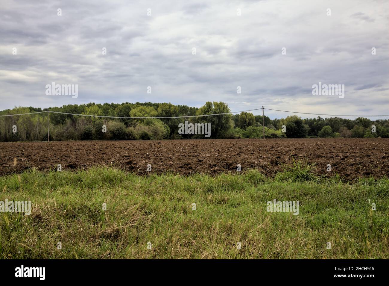 Piloni elettrici e linee elettriche in un campo arato in una giornata nuvolosa in autunno Foto Stock