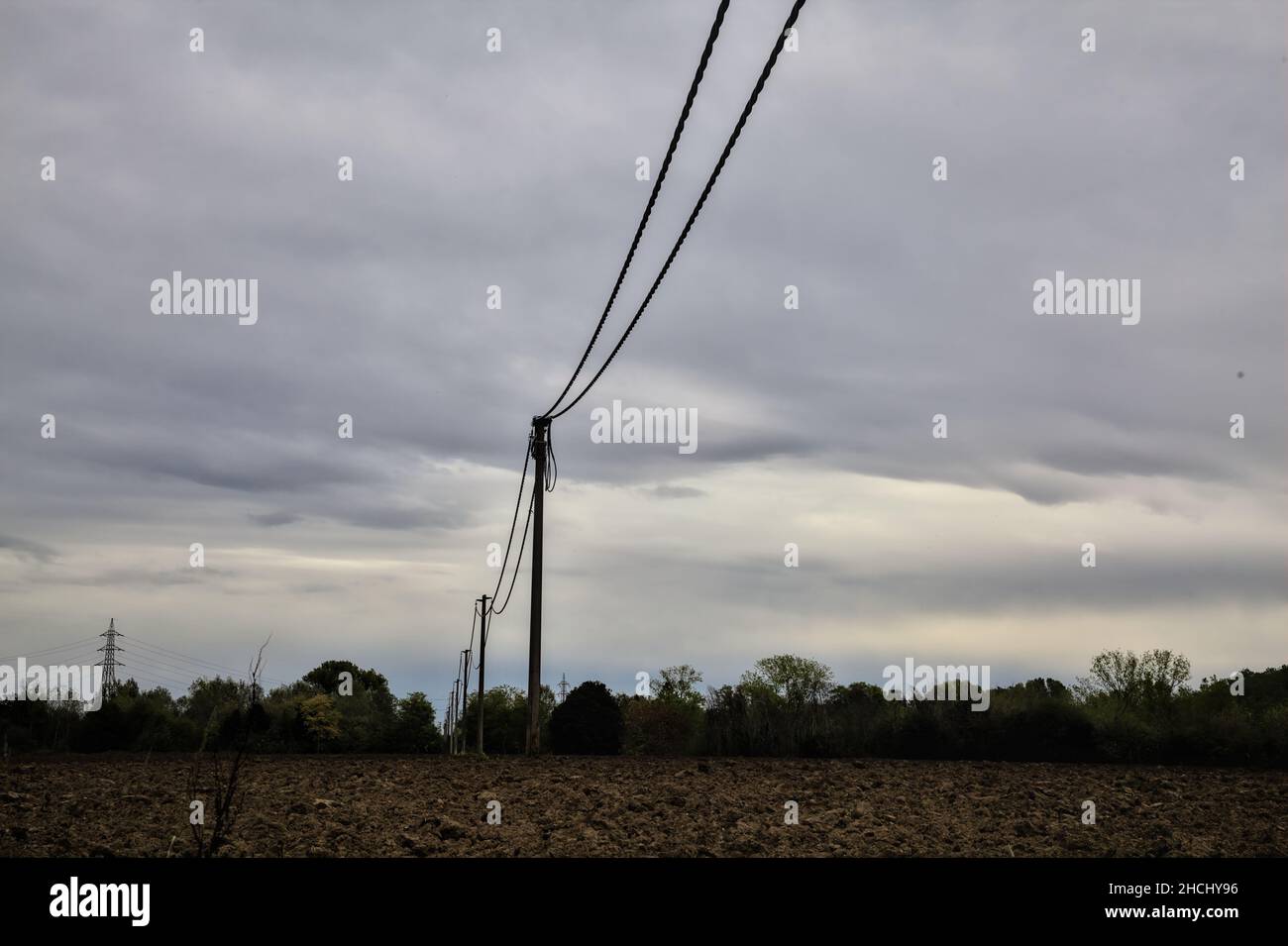 Piloni elettrici e linee elettriche in un campo arato in una giornata nuvolosa in autunno Foto Stock