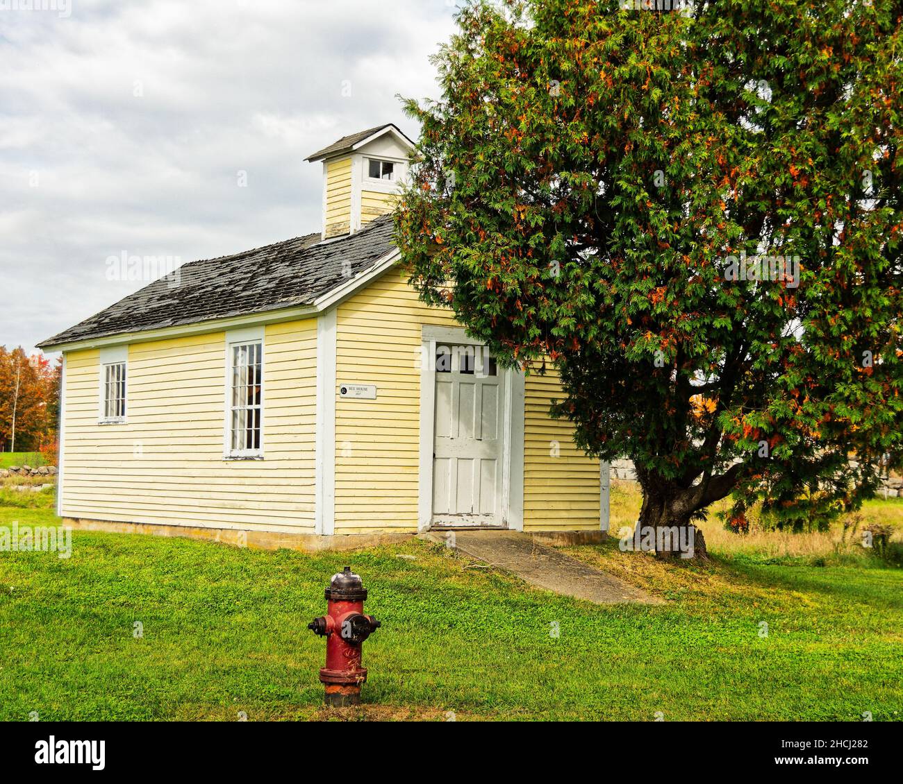 La casa di api gialle e legno rosso contro alberi autunnali in un giorno di caduta overcast. Canterbury Shaker Village, New Hampshire USA. Foto Stock