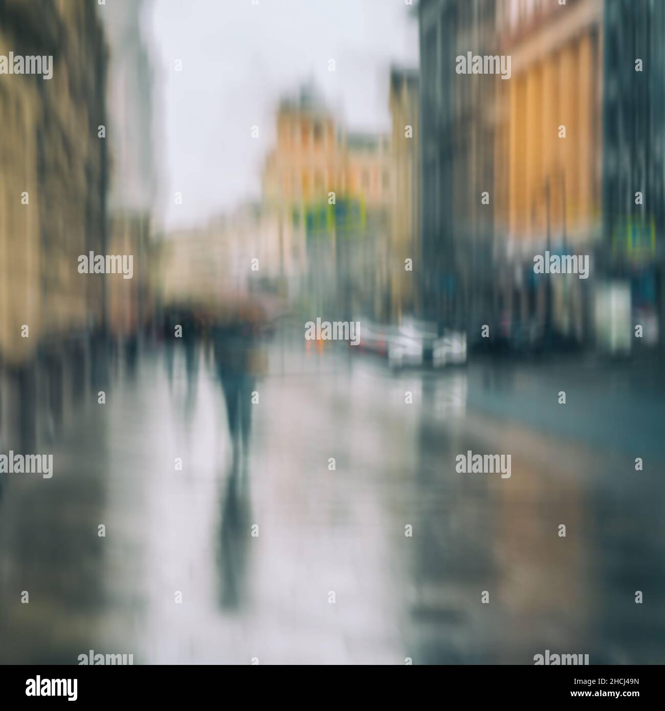 Serata piovosa in città. Silhouette di persone solitarie sotto l'ombrello. Sfondo astratto. Sfocatura intenzionale del movimento. Foto Stock