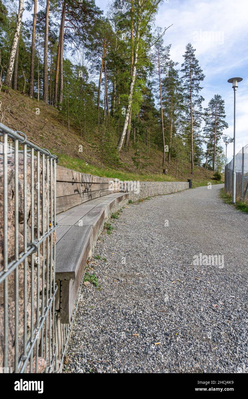Sodertalje, Svezia - 11 maggio 2021: Una recinzione speciale piena di pietre e panca curva in legno sul sentiero in Svezia Foto Stock