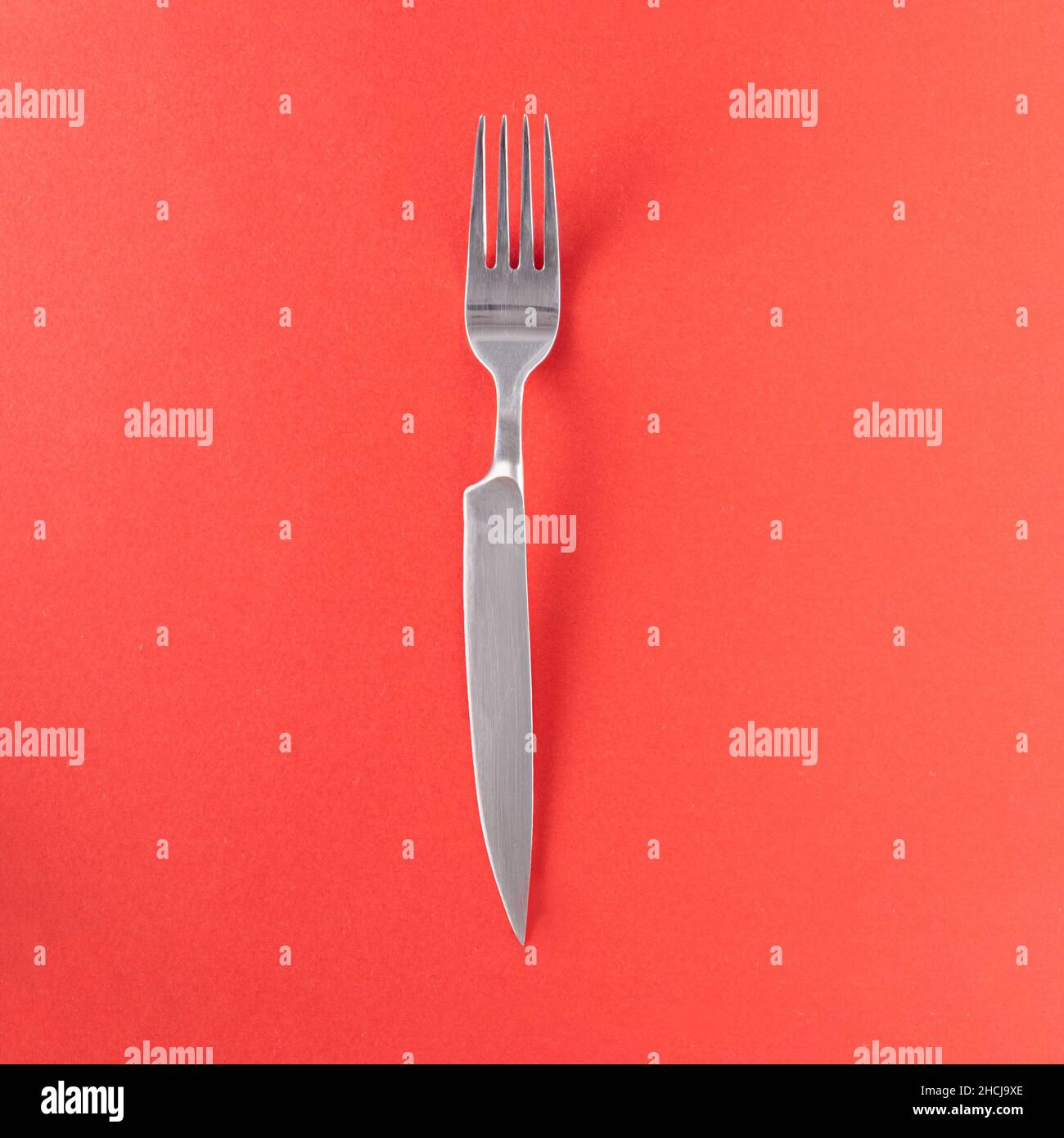 Forchetta con manico affilato contro sfondo rosso. Idea creativa a doppia lama. Composizione minima della posa piatta. Foto Stock