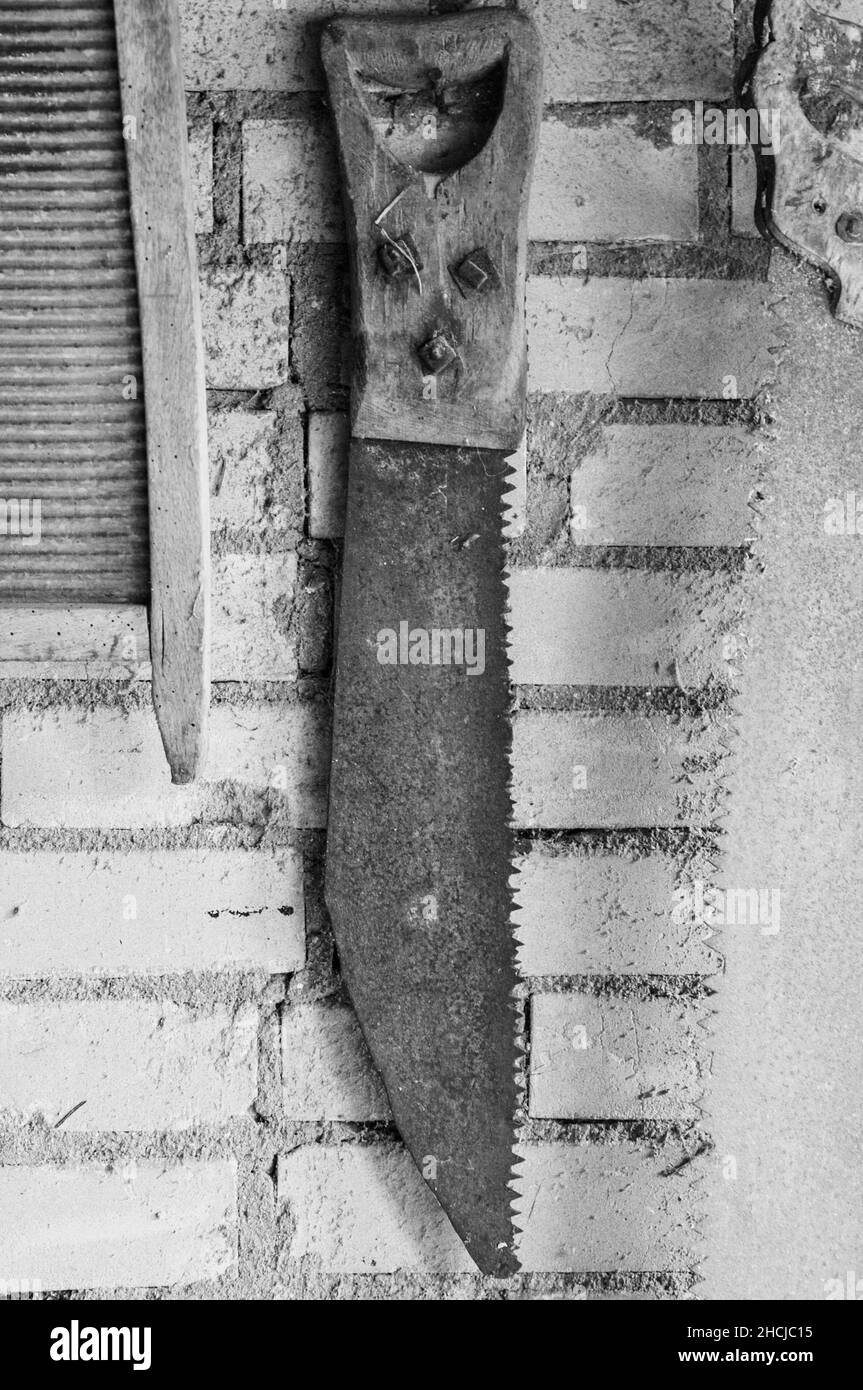 Scatto verticale in scala di grigi di una sega a mano arrugginita appesa a una parete Foto Stock