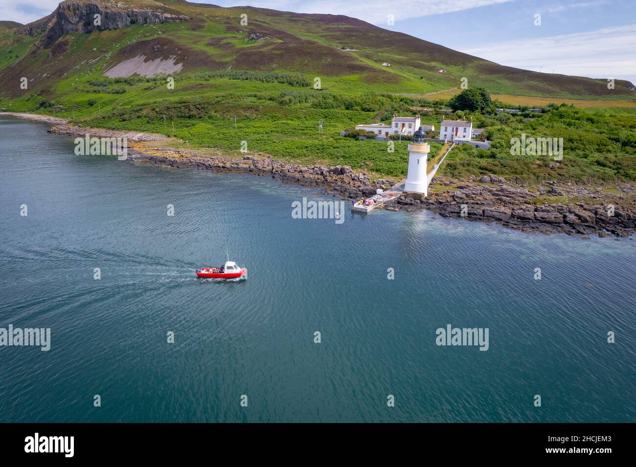 Piccolo traghetto rosso che arriva a un faro remoto Foto Stock