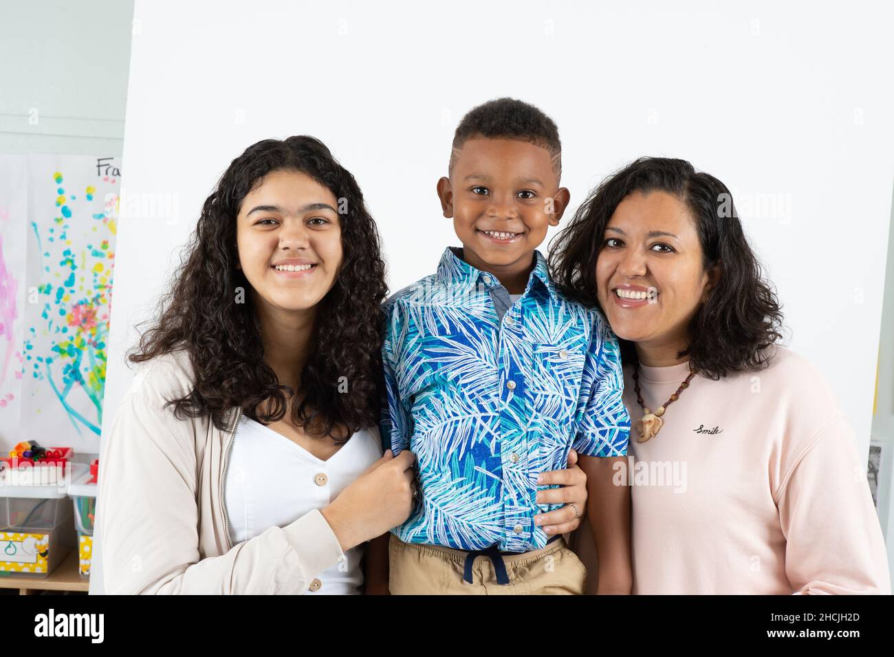Ritratto closeup di ragazzo di 5 anni, sorridente, sfondo bianco, con madre e sorella di 13 anni Foto Stock