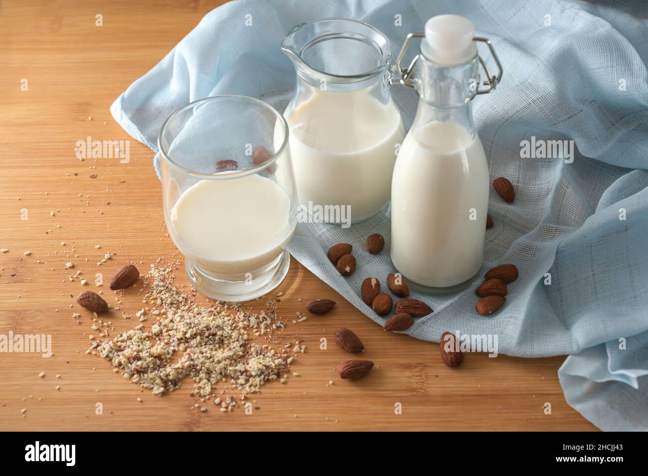 Latte vegano di mandorle in vasetti di vetro su un tovagliolo blu e una tavola di legno, alternativa rispettosa dell'ambiente ai prodotti lattiero-caseari di origine animale, spazio per copie, Foto Stock